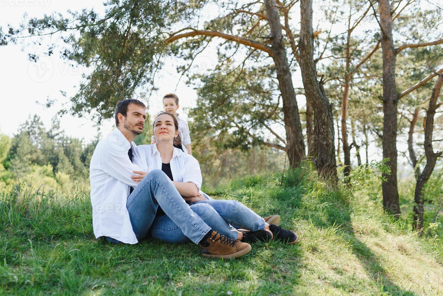 Lycklig ung familj utgifterna tid utomhus- på en sommar dag ha roligt på skön parkera i natur medan Sammanträde på de grön gräs. Lycklig familj. foto