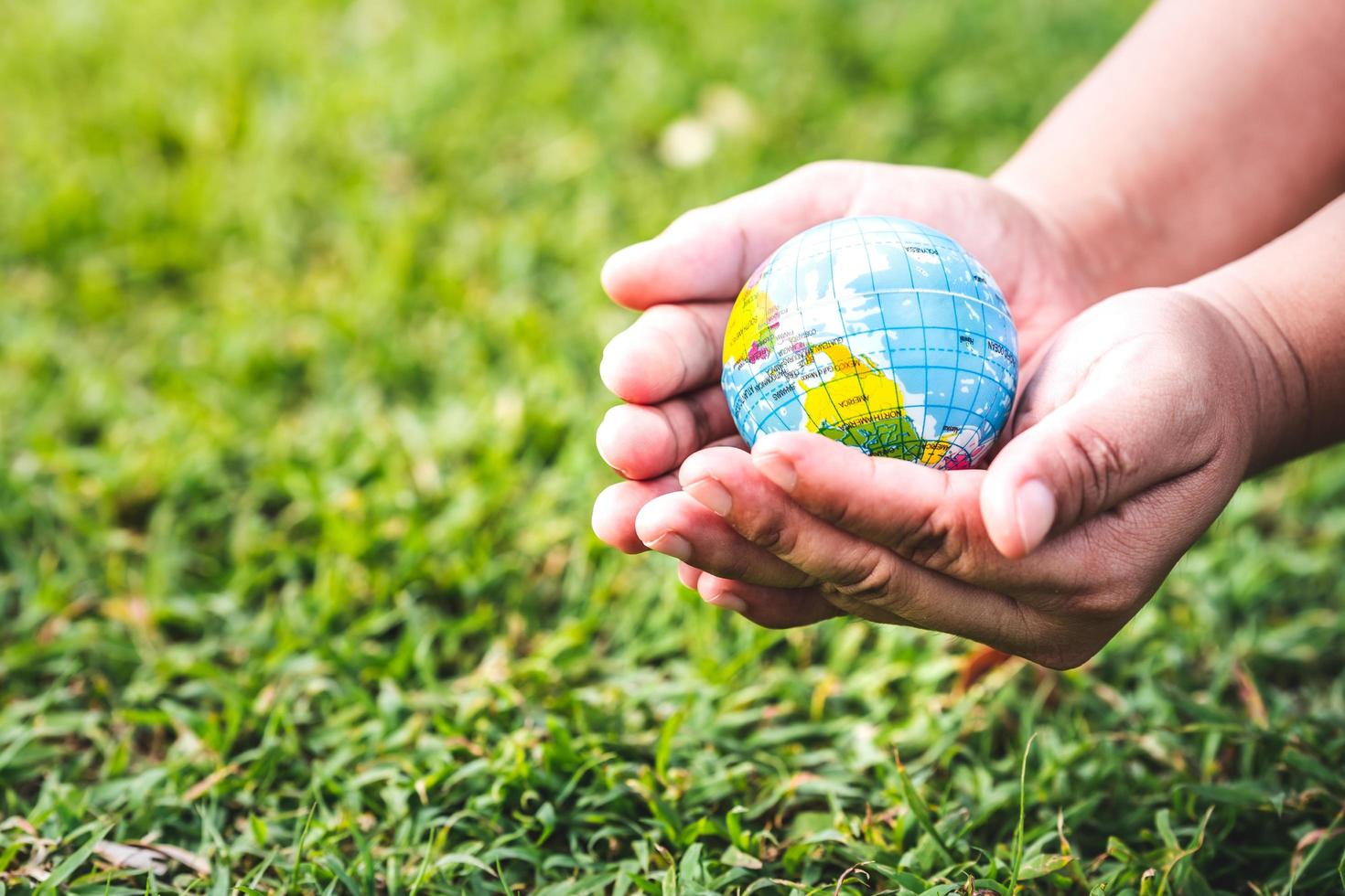 den mänskliga handen som skyddar vår planet. grön gräsmatta bakgrund. omfamna jorden. världs miljö dagen. e-co-vänligt koncept. foto