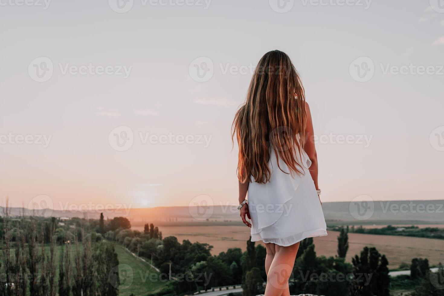 Lycklig kvinna stående med henne tillbaka på de solnedgång i natur i sommar med öppen händer. romantisk skön brud i vit boho klänning Framställ med bergen på solnedgång foto