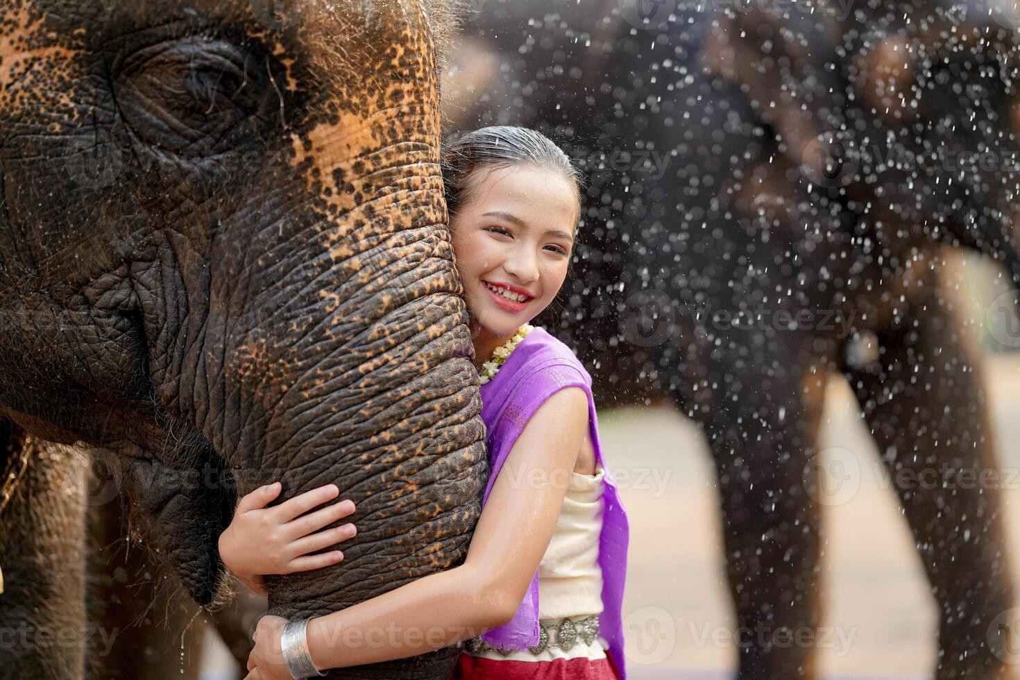 skön lantlig thai flicka ha på sig thai nordlig traditionell klänning kram trunk av asiatisk elefant med suddig av vatten spray och några elefant bakgrund. foto