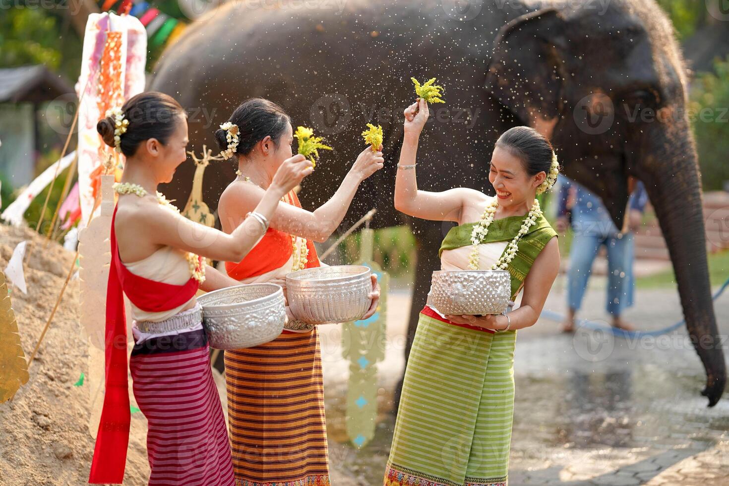 närbild skön thai ung lady gods thai traditionell klänning använda sig av blommor till stänk vatten på varje Övrig på de thai ny år dag i en roligt sätt på suddig elefant och lugg av sand bakgrund. foto