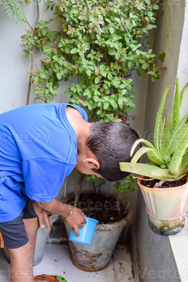 söt 5 år gammal asiatisk liten pojke är vattning de växt i de kastruller belägen på hus balkong, kärlek av ljuv liten pojke för de mor natur under vattning in i växter, unge plantering foto