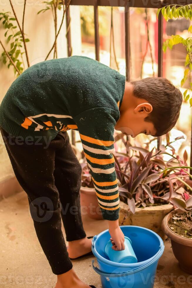 söt 5 år gammal asiatisk liten pojke är vattning de växt i de kastruller belägen på hus balkong, kärlek av ljuv liten pojke för de mor natur under vattning in i växter, unge plantering foto