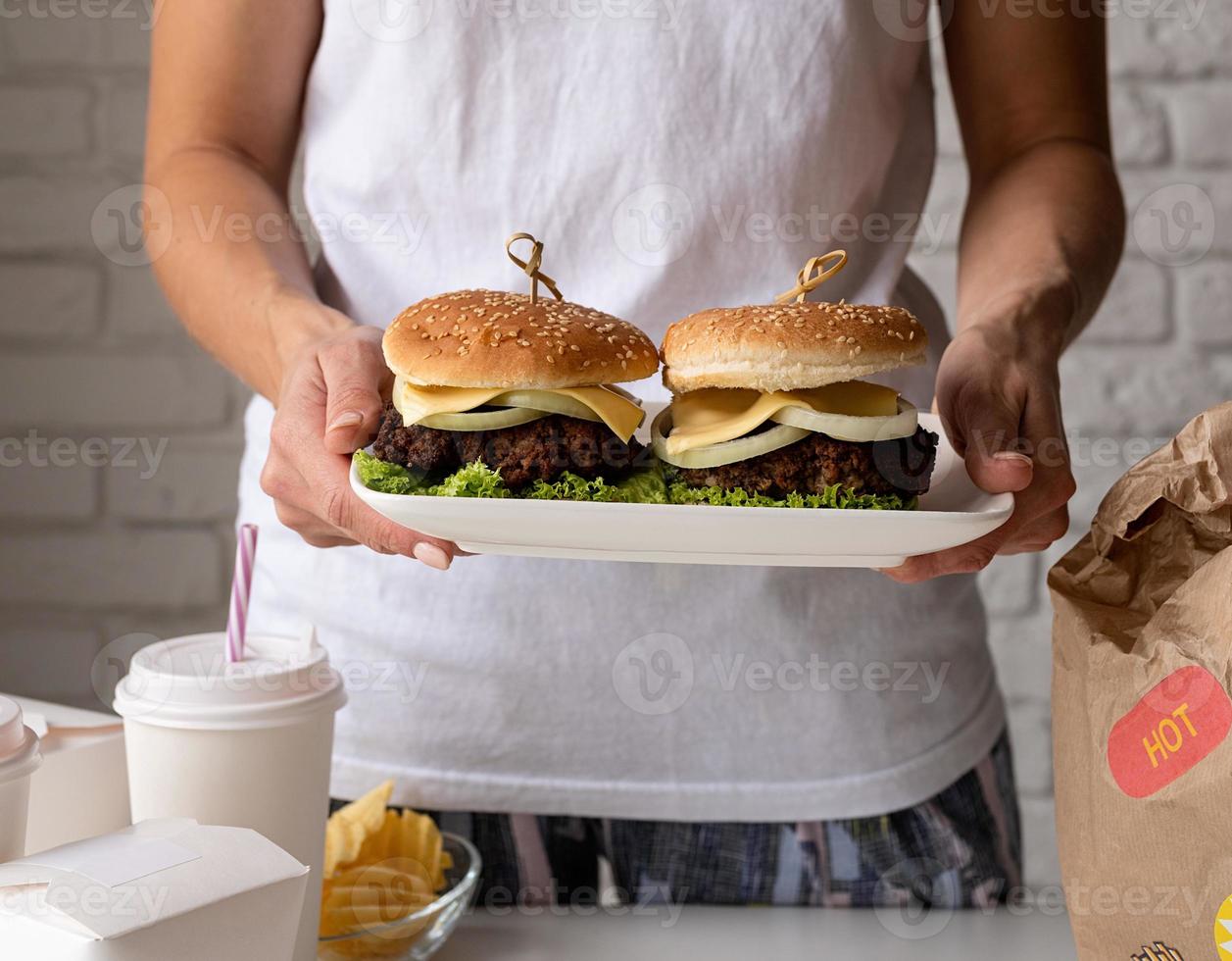 kvinna i hemmakläder packar upp mat hemleverans med hamburgare, nudelådor och drycker foto