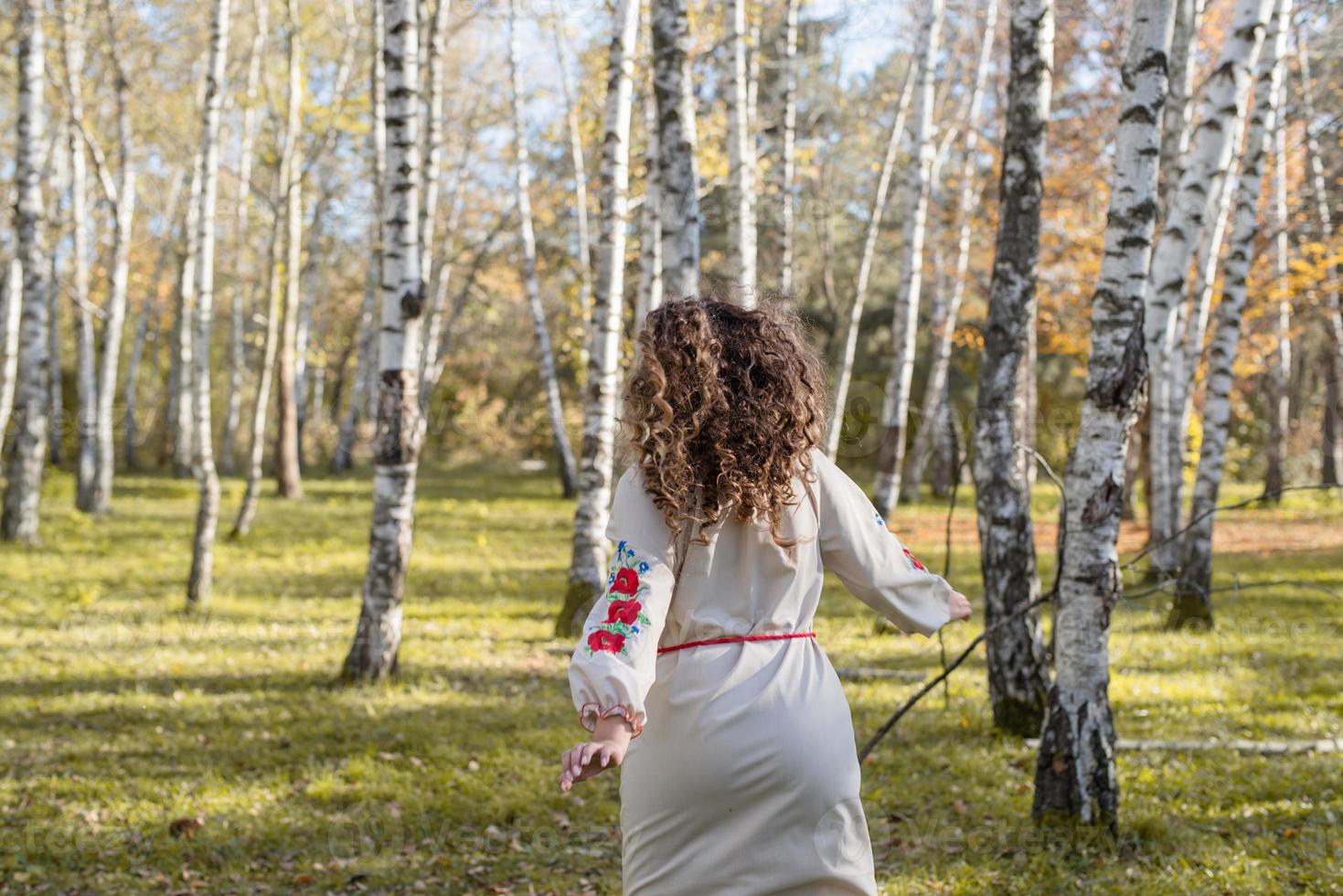 vacker kvinna i ukrainska nationella traditionella kostymkläder dansar i skogen foto