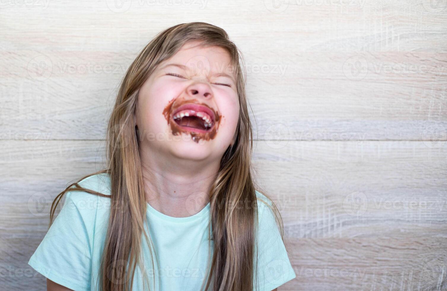 Lycklig och skrattande liten flicka äter choklad smutsig ansikte. stänga upp av unge med smutsig ansikte i choklad . foto