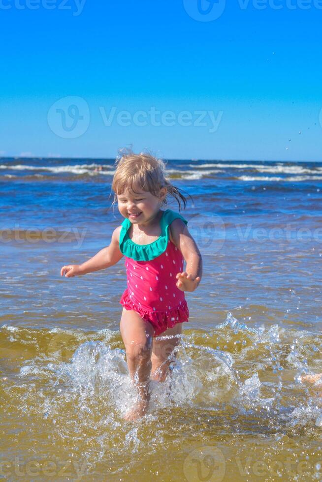 ung Lycklig barn flicka av europeisk utseende ålder av 4 har roligt i vatten på de strand och stänk, tropiskt sommar yrken, helgdagar.a barn åtnjuter de hav.vertikal Foto. foto