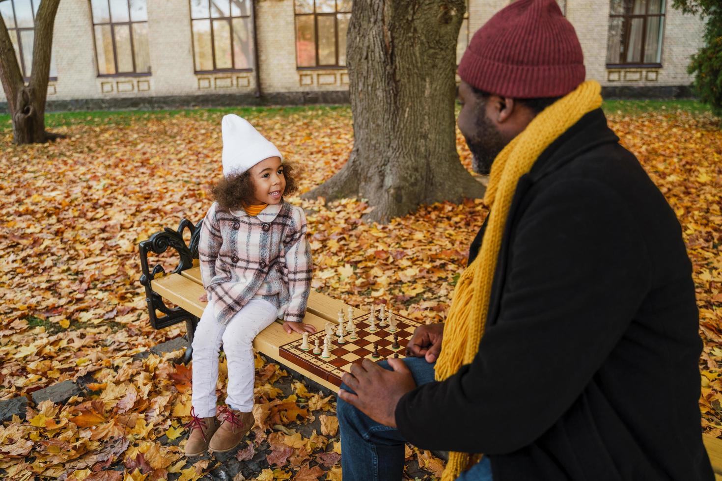 svart farfar och barnbarn spelar schack i höst park foto
