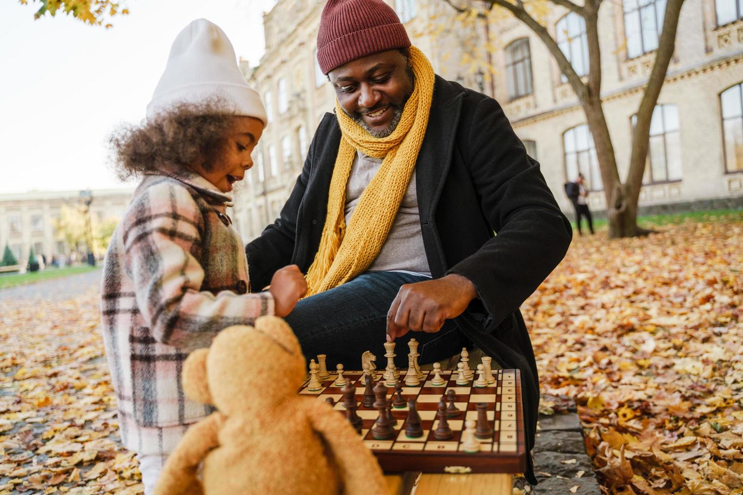 svart farfar och barnbarn spelar schack i höst park foto