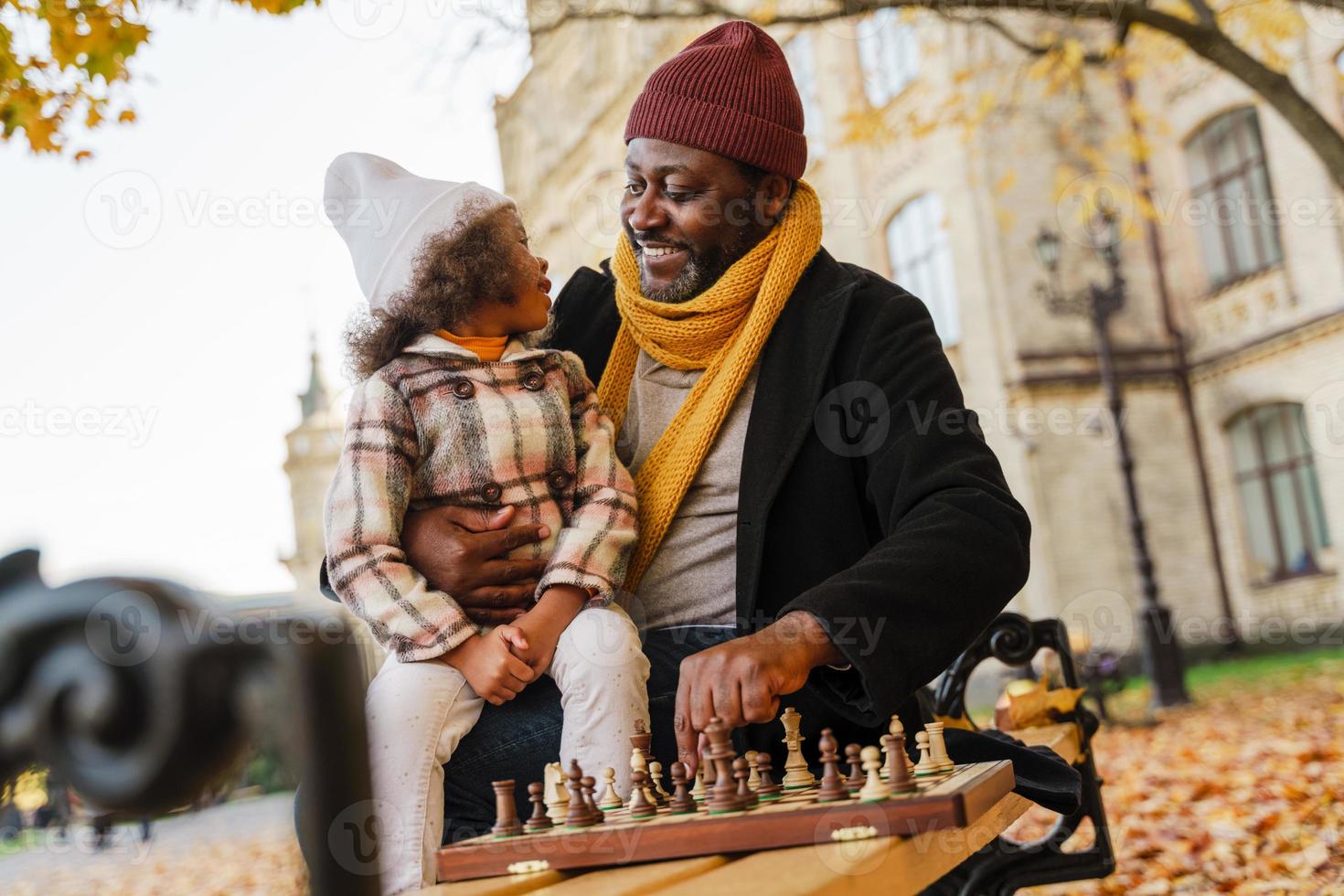 svart farfar och barnbarn spelar schack i höst park foto