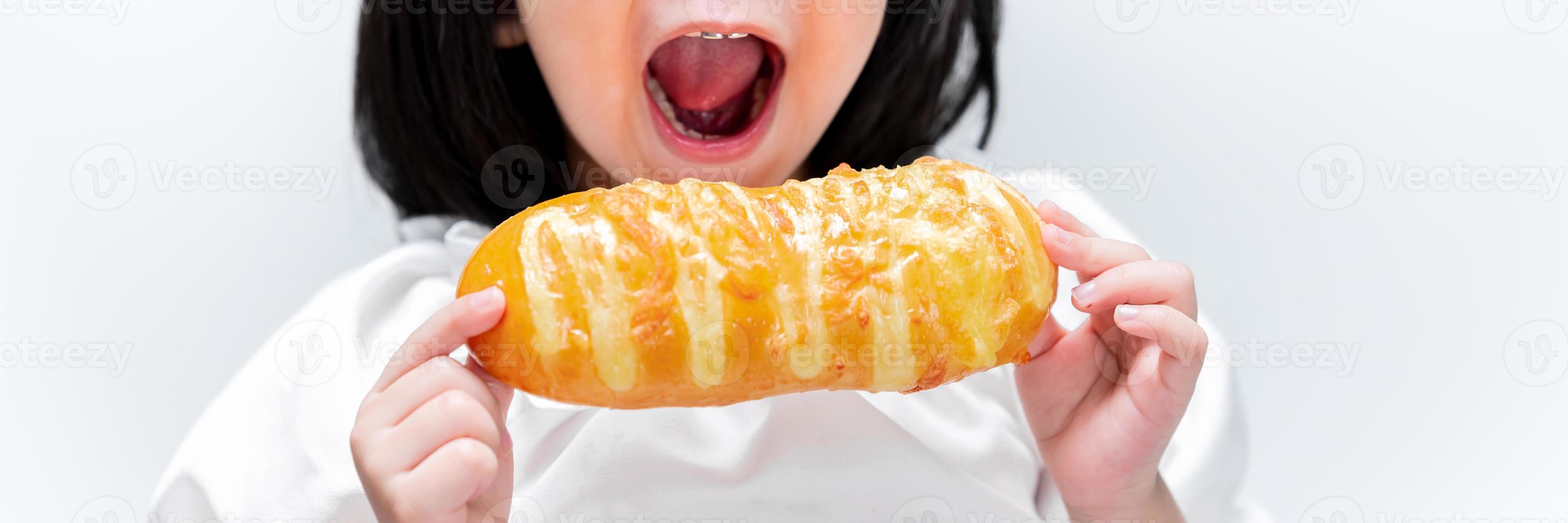 liten flicka äter gott bröd. barn äter rostat bröd till frukost. närbild bild. ungen öppnar munnen för att bita i maten. foto