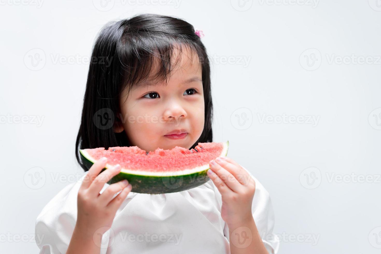 porträtt av vacker svarthårig liten flicka som äter röd vattenmelon hälsosam frukt mellanmål. bedårande asiatiska barn håller vegetabilisk mat. på isolerade vit bakgrund. foto