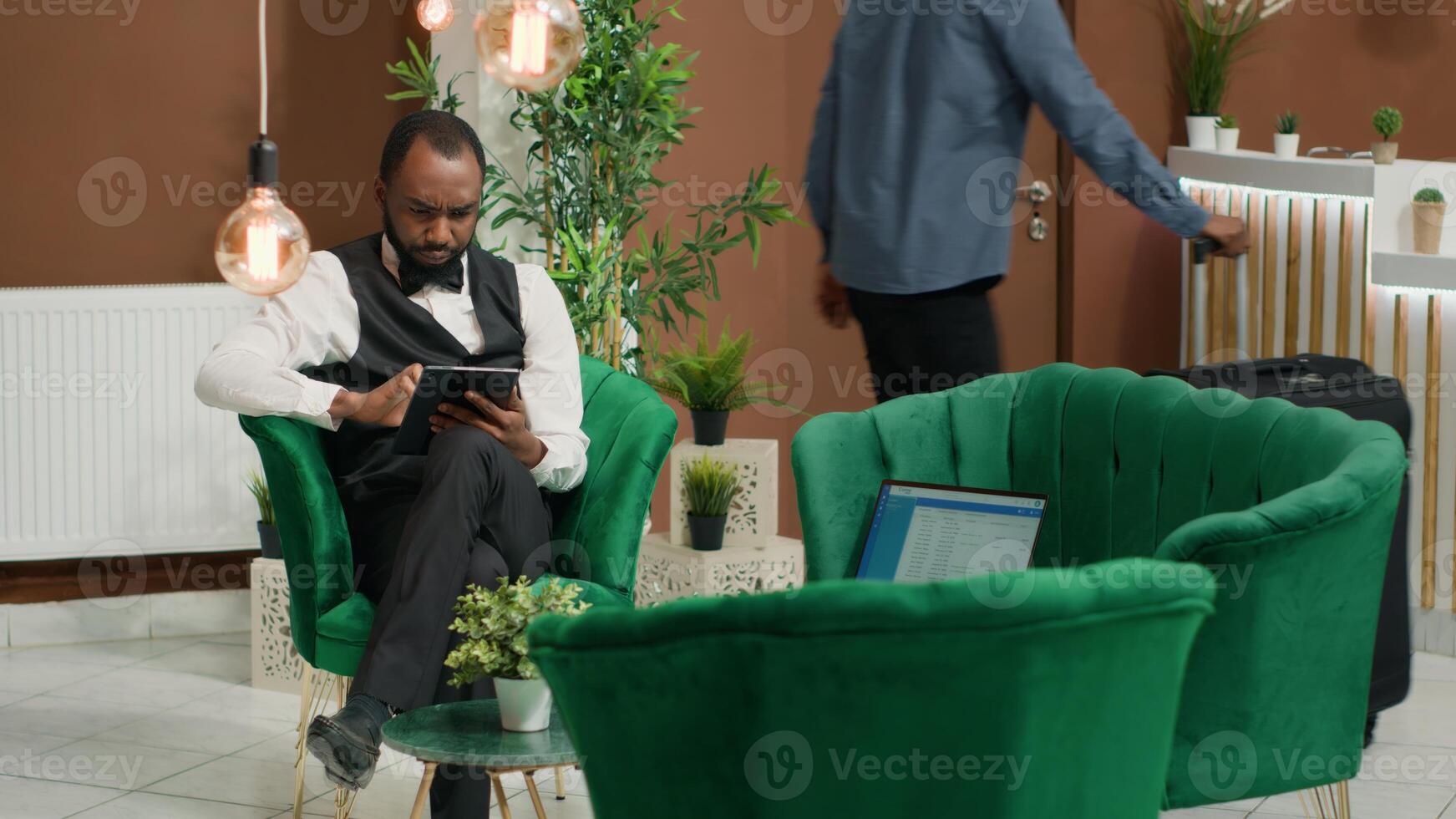 afrikansk amerikan hotell personal bär enhetlig i lobby använder sig av digital läsplatta till hjälp klara av uppkopplad rum bokningar. piccolo innehav elektronisk enhet som förs in i detaljer för kommande reservationer. foto