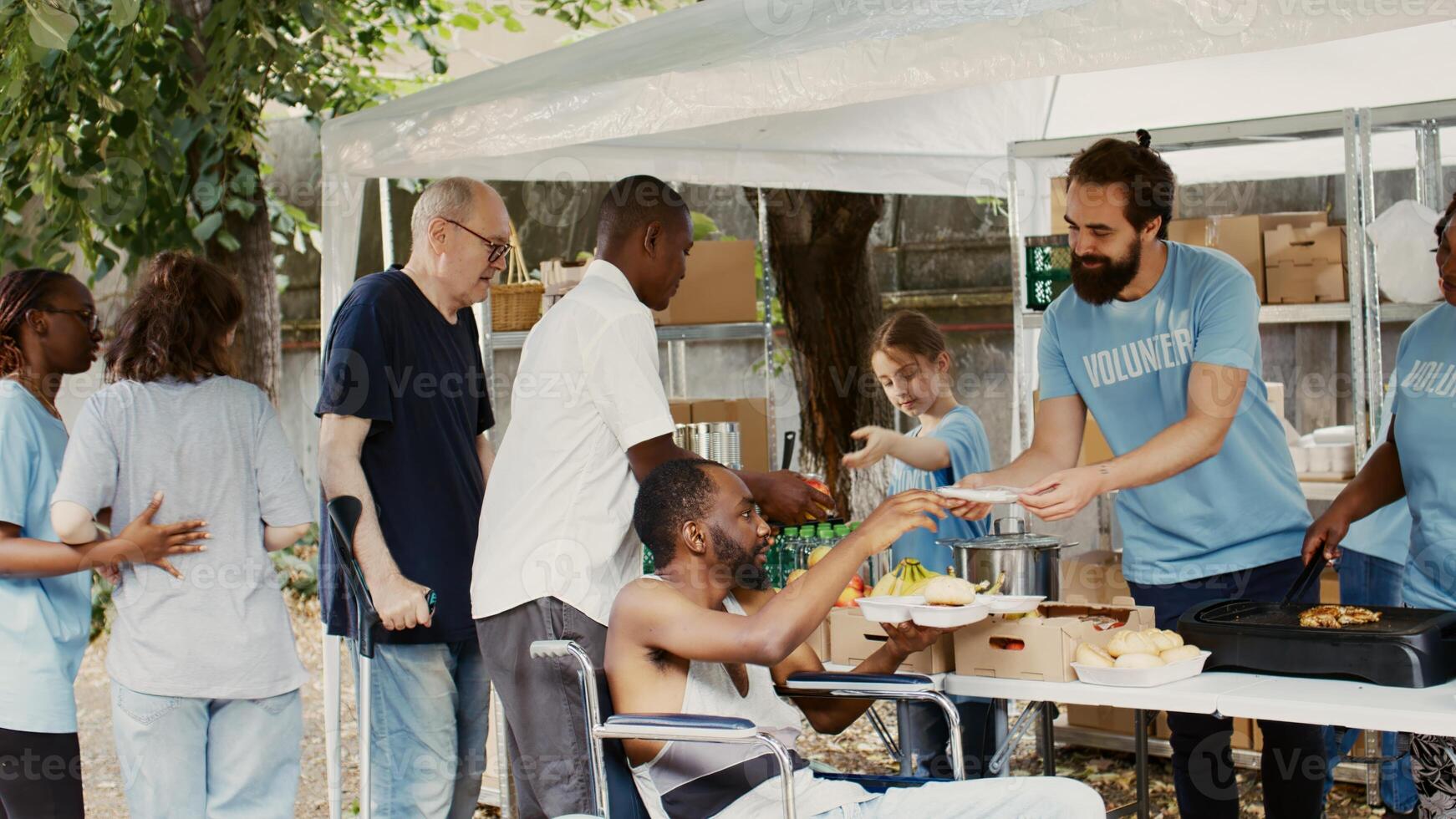 humanitär hjälpa team tillhandahålla bistånd till de handikappade, fattig och hemlös människor. välgörenhet arbetare ger bort fri mat till svart man i rullstol möte hans behov medan andra vänta i linje. foto