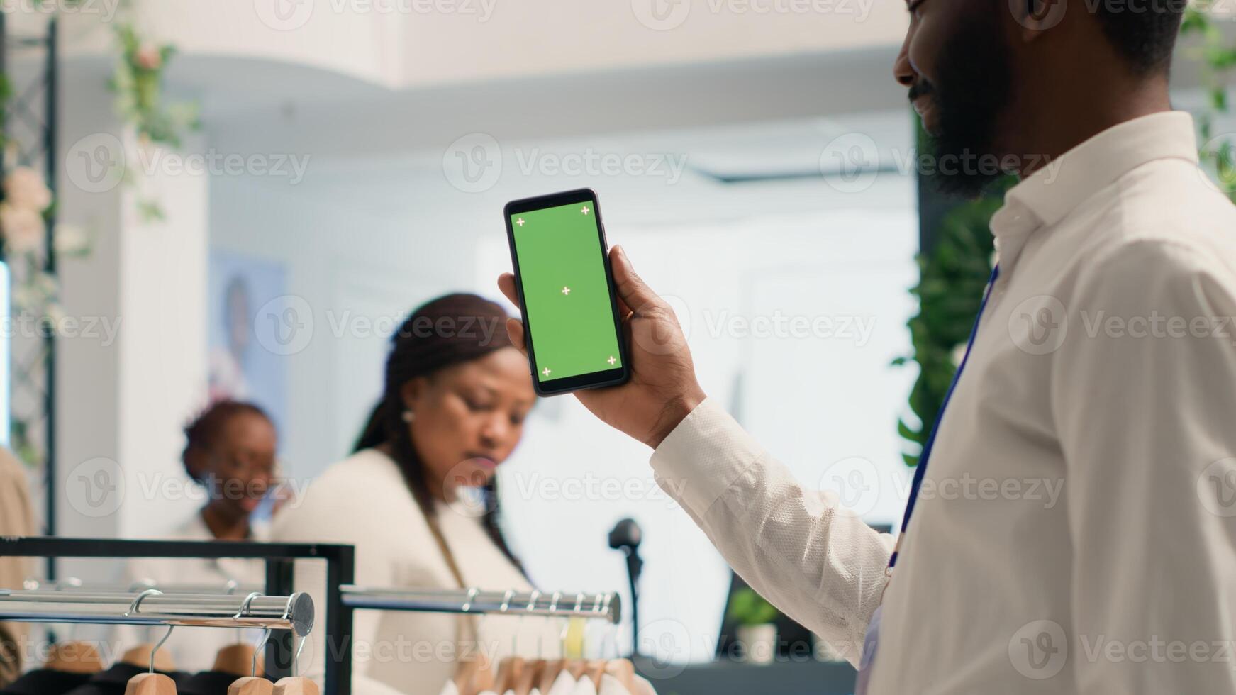 afrikansk amerikan man innehav attrapp mobiltelefon i premie Kläder Lagra med eleganta formell klädsel kläder. bipoc kund med grön skärm mobil telefon i designer utställningslokal foto