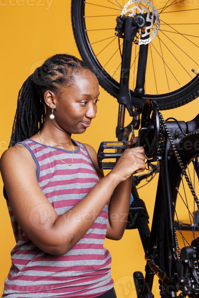 engagerad svart kvinna i närbild skott använder sig av expert- verktyg till reparera och fixera cykel vev ärm. detaljerad se av sportig afrikansk amerikan kvinna lagning skadad cykel förbi använda professionell multiverktyg. foto