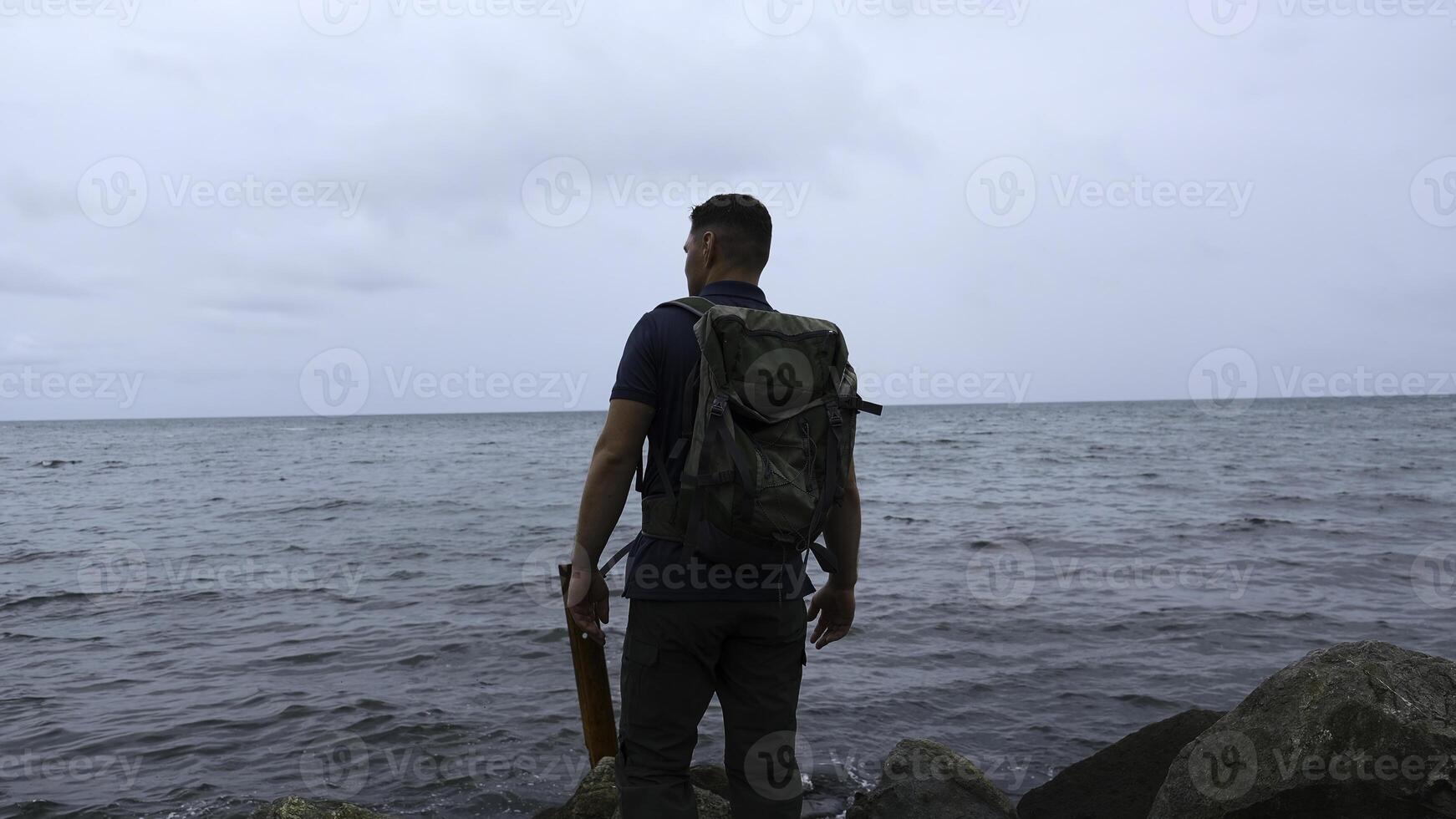 man promenader på sten kust på bakgrund av hav. klämma. man promenader på stenar av hav vägbank på molnig dag. promenad längs hav sten kust på molnig dag foto