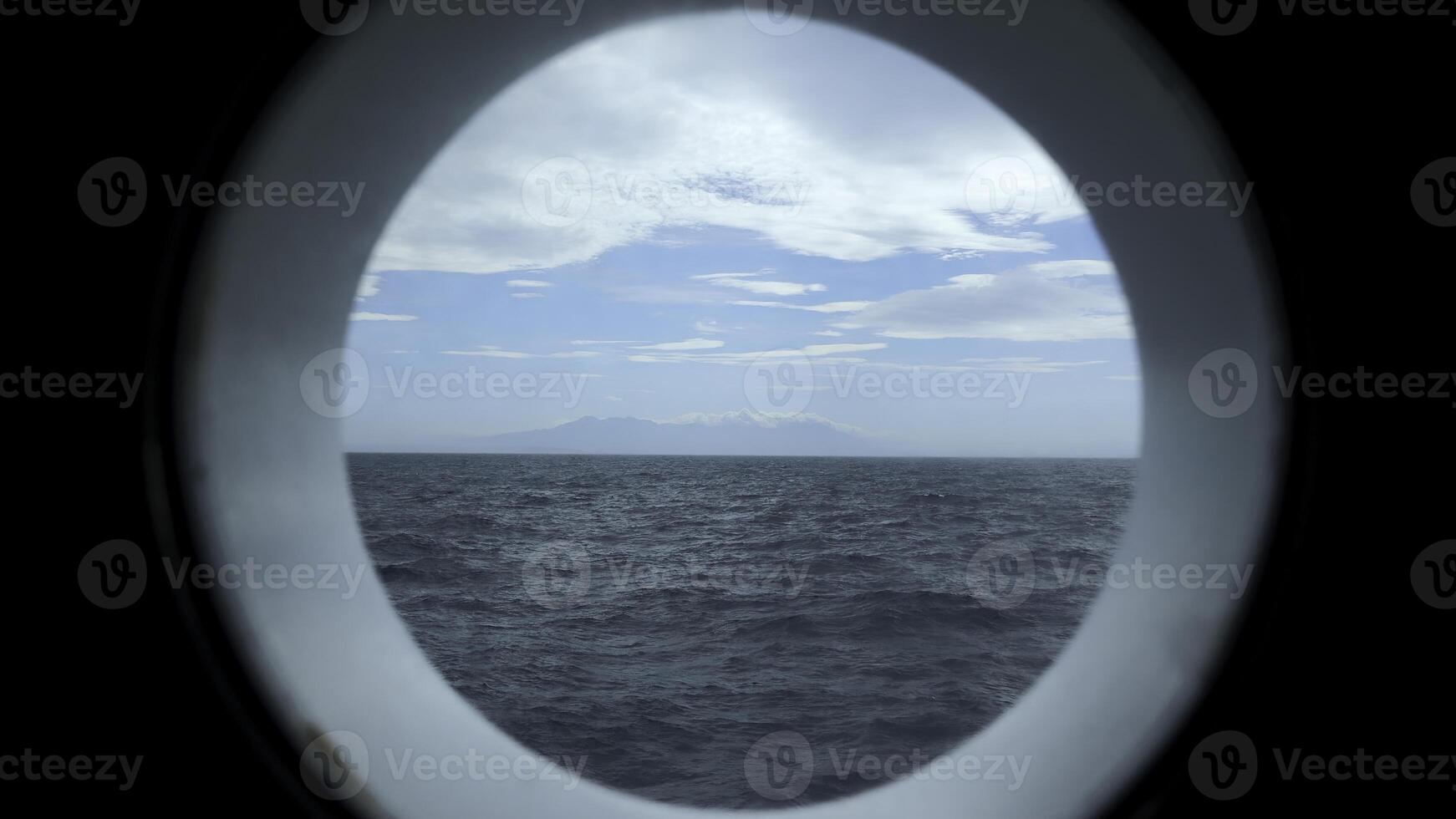 se från runda däck fönster till hav. klämma. skön marinmålning med berg kust på horisont från runda fönster. hav resa och se från runda fönster foto