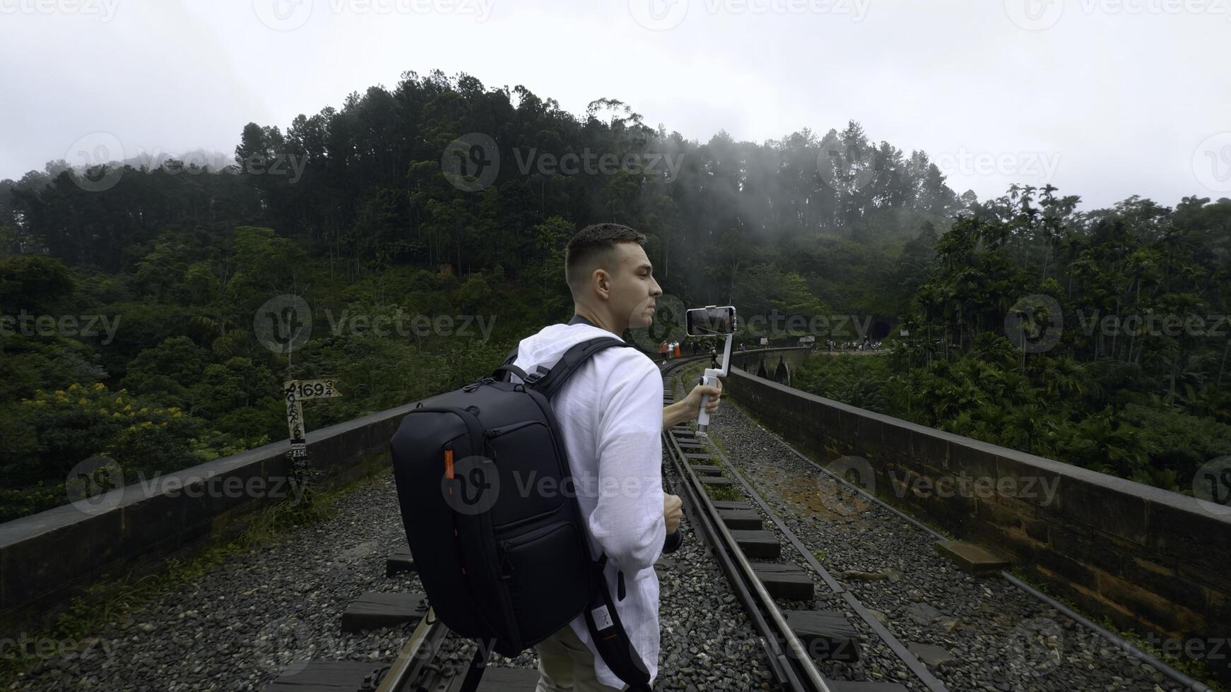 bak- se av en man turist tar bilder av berg skog landskap på smartphone. handling. vandrare gående på järnvägar. foto