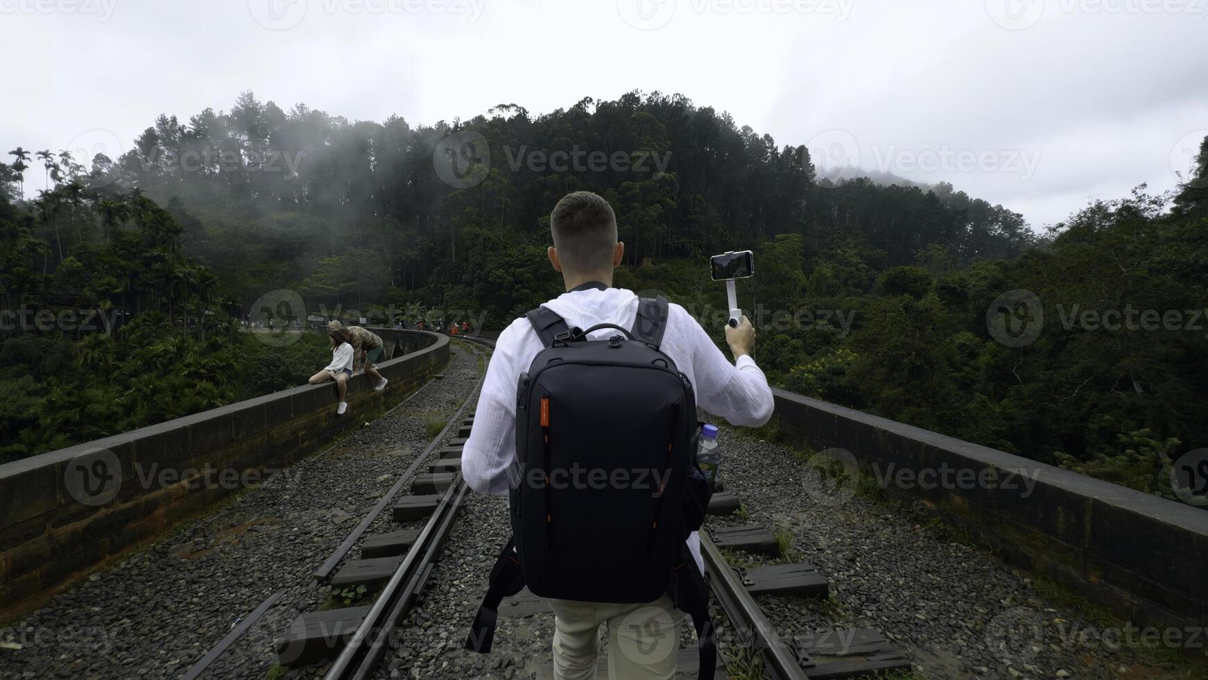 caucasian resande man inspelning video av grön berg landskap. handling. man gående på järnväg med ryggsäck. foto
