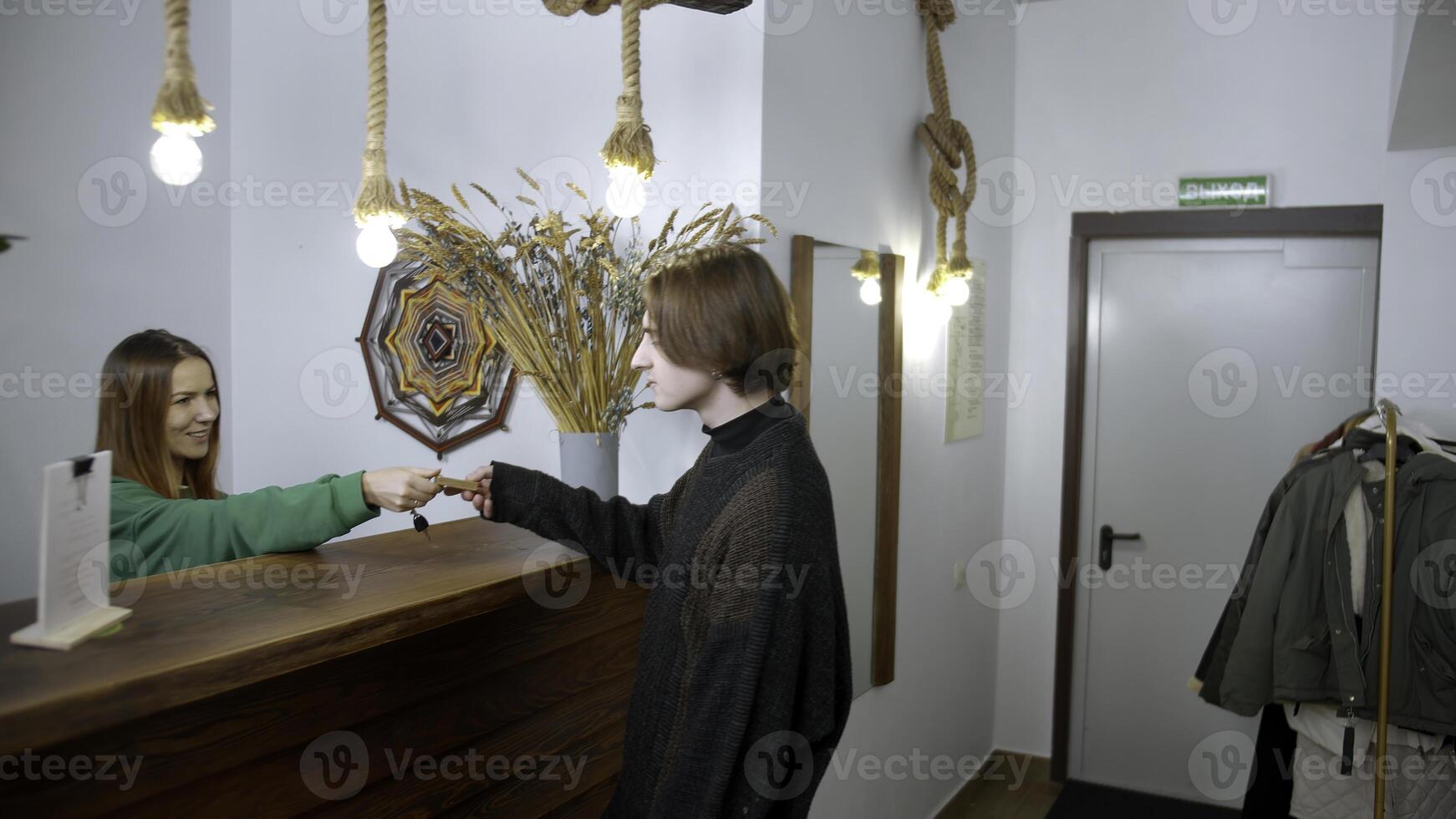 ung man kolla upp i på en hotell. media. Lycklig receptionist ger en nyckel till en man på de reception skrivbord, begrepp av reser. foto