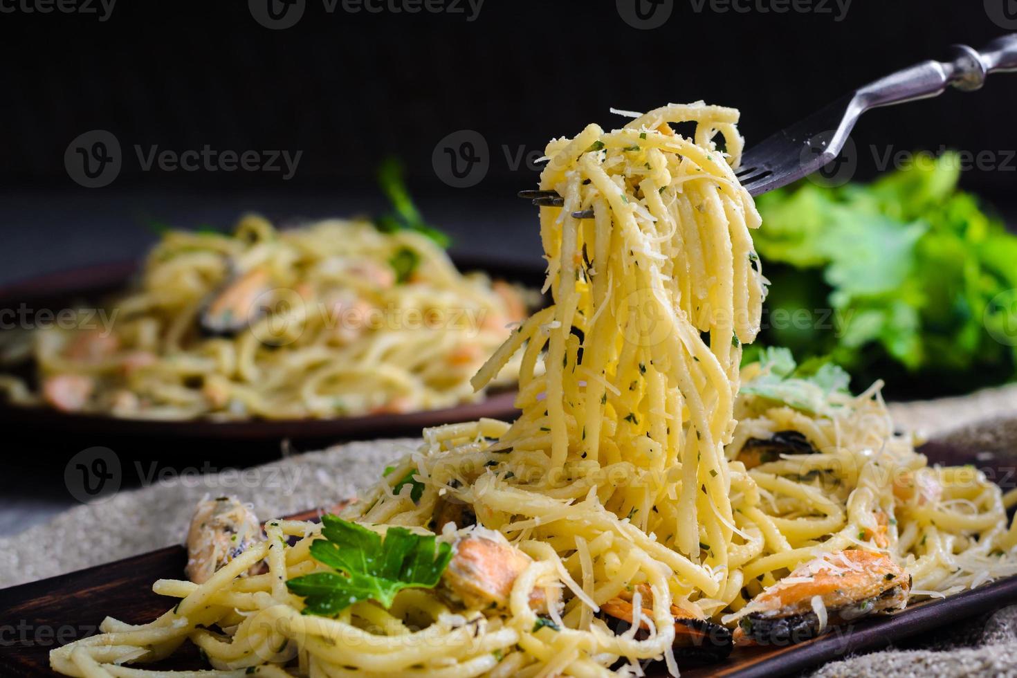 en man tar en gaffel med en gaffel från en tallrik på ett träbord. pasta med skaldjur, räkor och musslor i krämig sås. foto