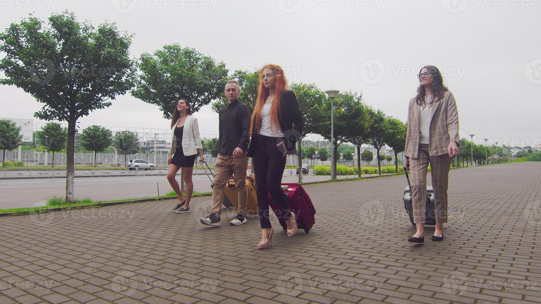 grupp av turister gående med bagage på de bakgrund av de flygplats terminal. en grupp av ung affärsmän med bagage flög till en ny stad och promenad mot de bakgrund av en ny modern flygplats foto