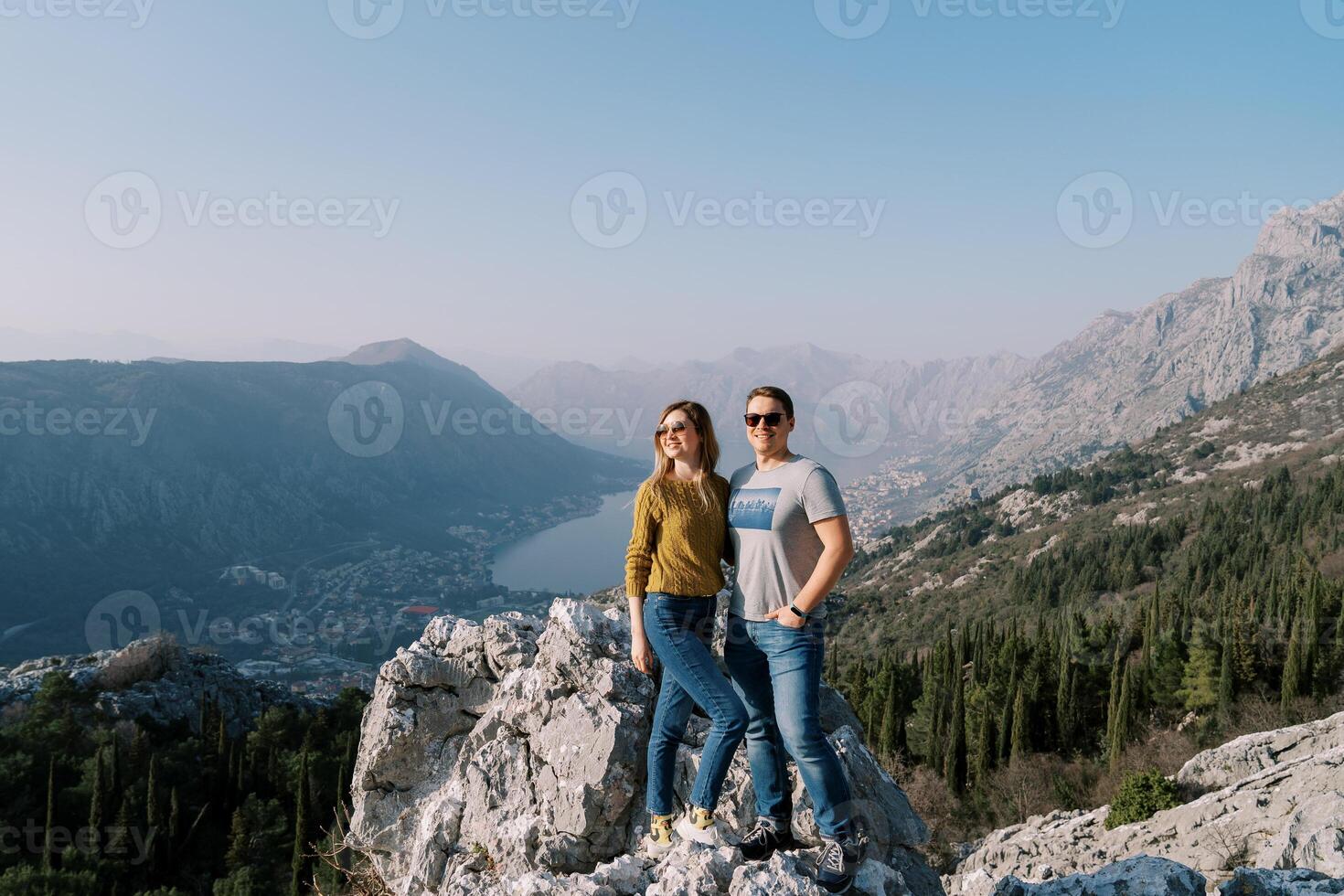 leende man kramar kvinna på en sten ovan de bukt av kotor. monte foto