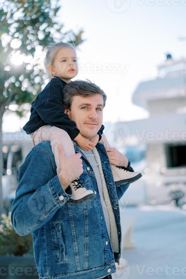 pappa med en liten flicka på hans axlar står på de promenaden motsatt de förtöjd båtar foto