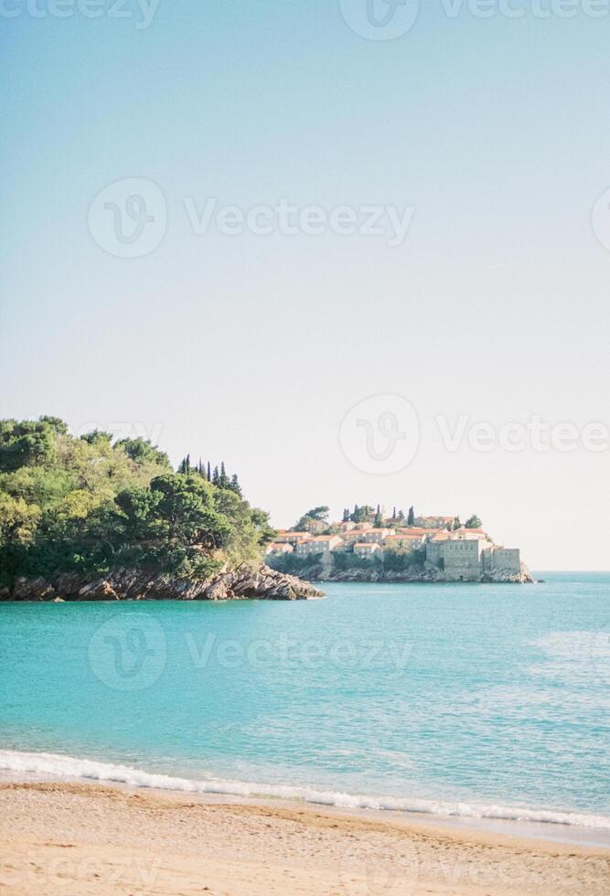 se från de sandig strand av de ö av sveti stefan, ser ut från Bakom en trädbevuxen klippa. monte foto