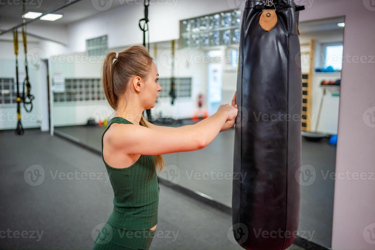 ung kvinna står Nästa till en svart boxning päron till låta av ånga i Gym. hög kvalitet Foto
