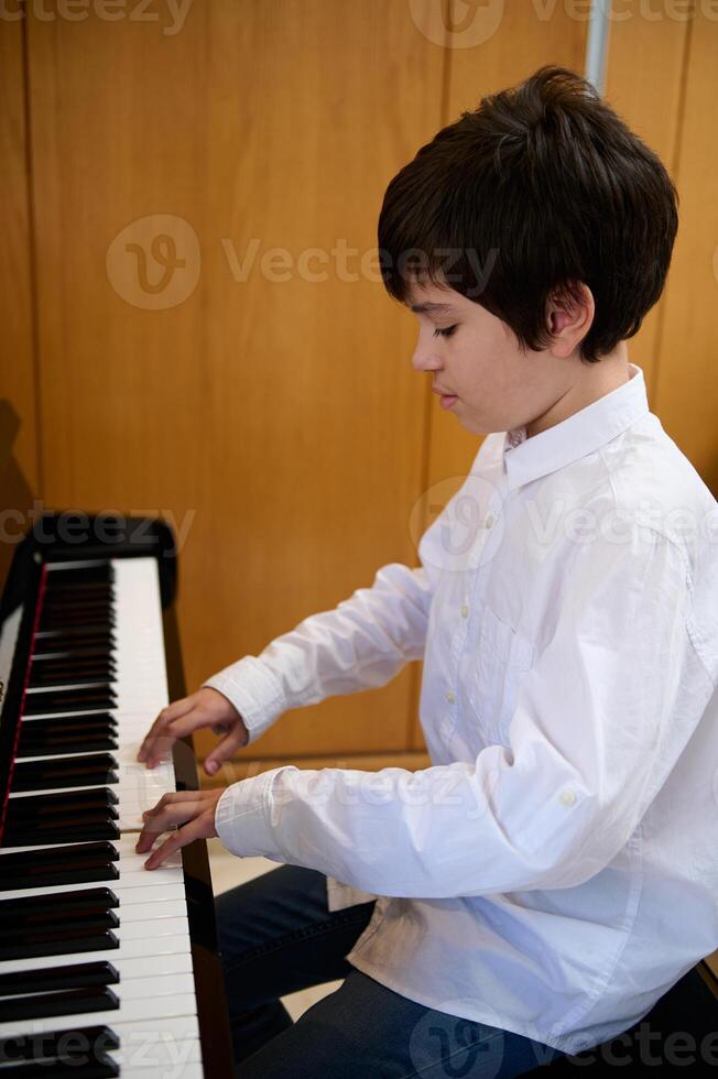 porträtt av tonåring pojke pianist sätta fingrar på piano nycklar, spelar piano, njuter de prestanda av klassisk musik foto