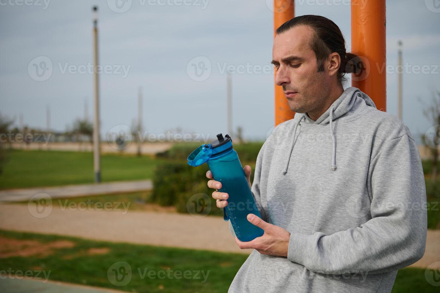 atletisk man innehav en flaska av isoton vatten, vilar efter tung träna på de urban idrottsplats. människor och sport foto