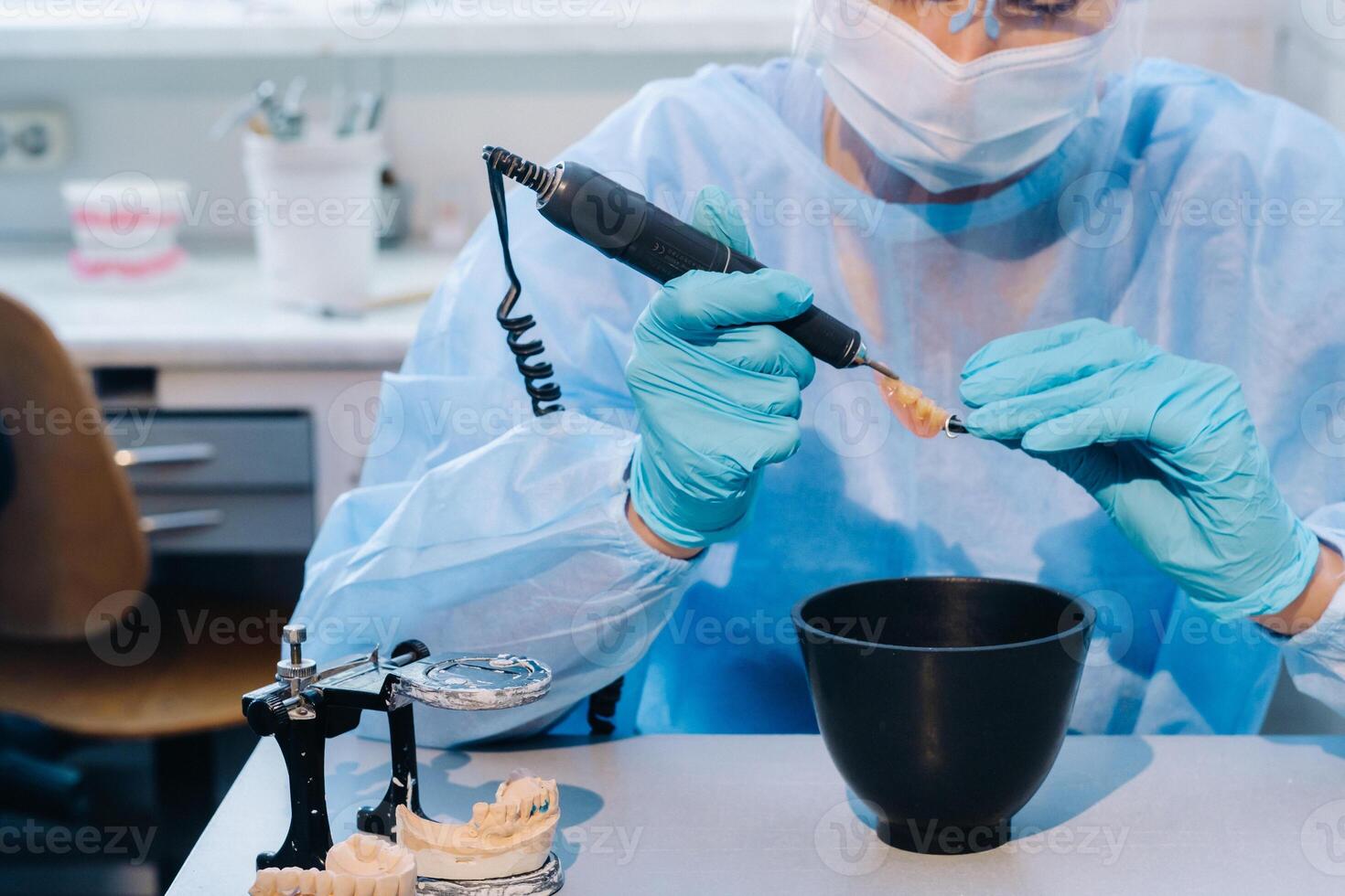 en dental tekniker i skyddande Kläder är arbetssätt på en protes- tand i hans laboratorium foto