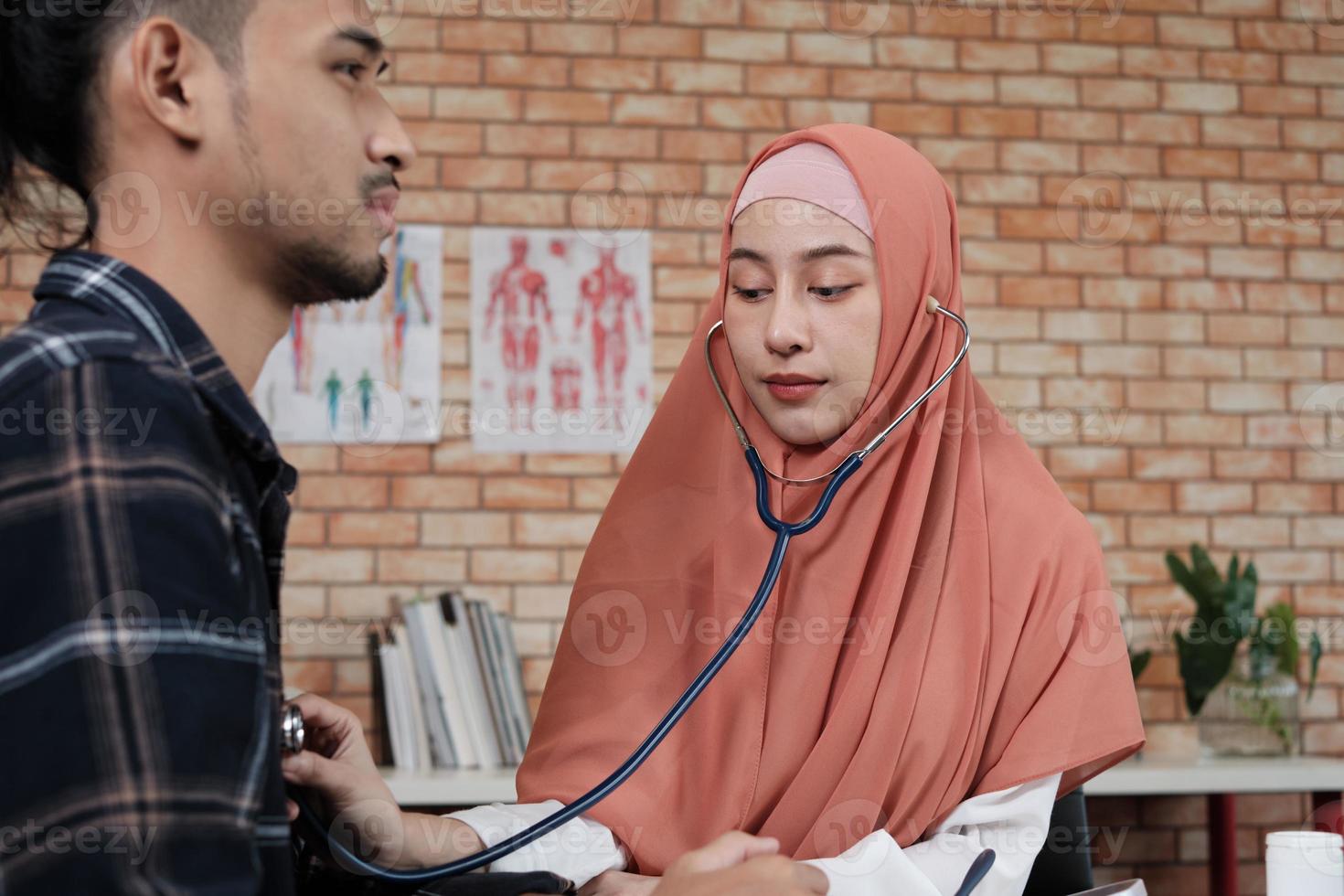 ung vacker kvinnlig läkare är hälsoundersökning manlig patient på kontoret på sjukhuskliniken och rådgör med ett leende om läkemedel. denna asiatiska medicinska specialist är en islamisk person som bär hijab. foto