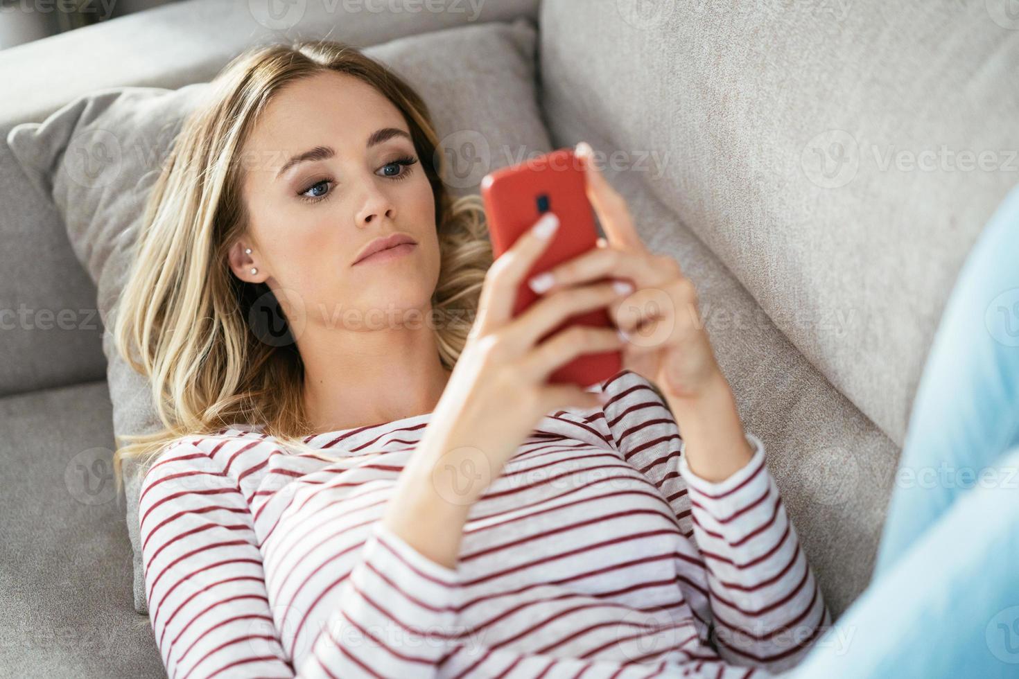 ung blond kvinna med sin smartphone liggande på soffan. foto