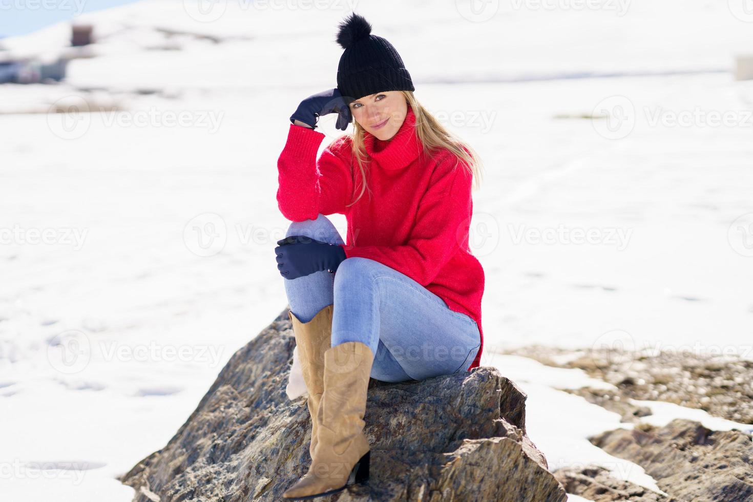 blond kvinna sitter på en sten i de snöiga bergen på vintern, i Sierra Nevada, Granada, Spanien. foto