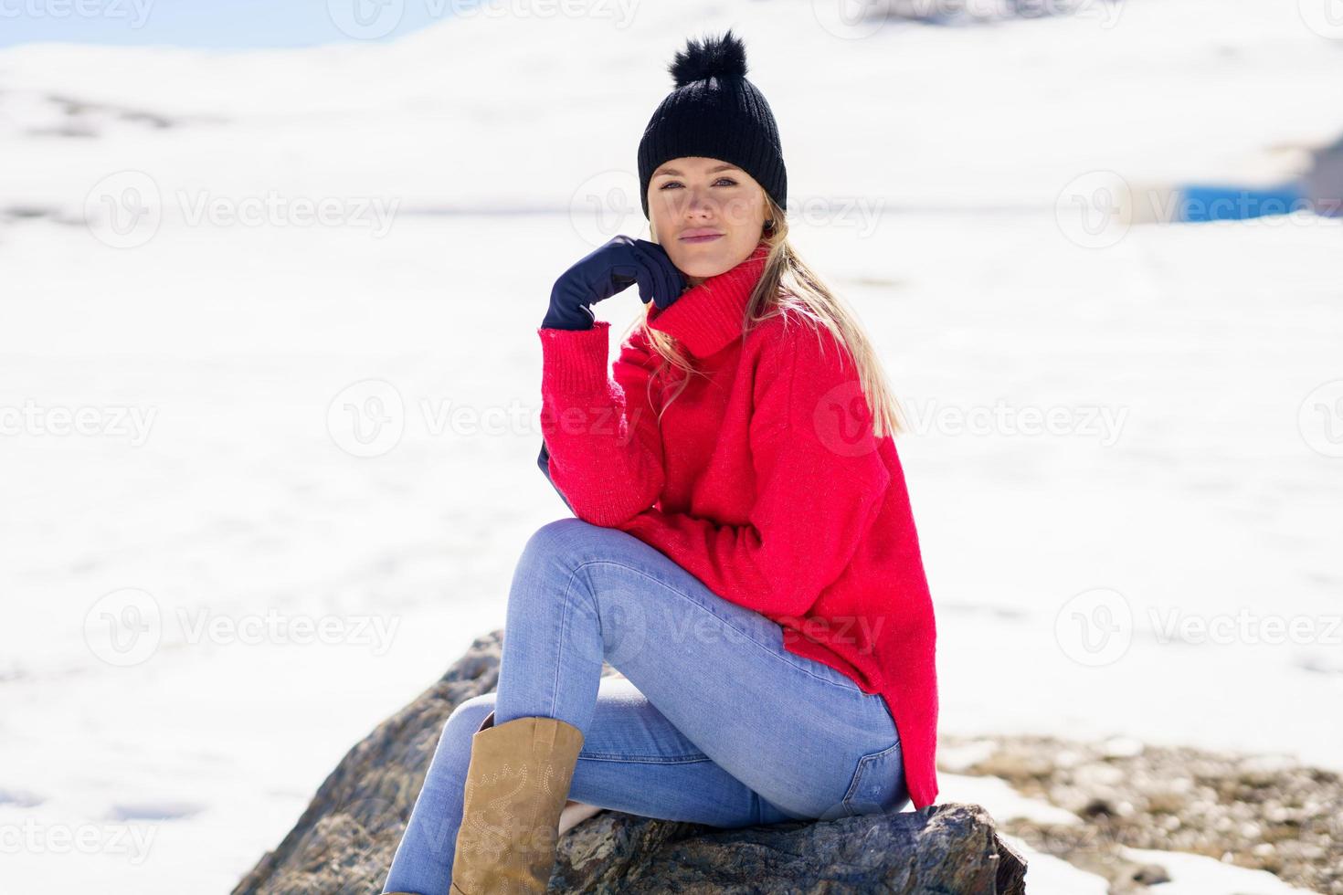 ung kvinna sitter på en sten i de snöiga bergen på vintern, i Sierra Nevada, Granada, Spanien. foto