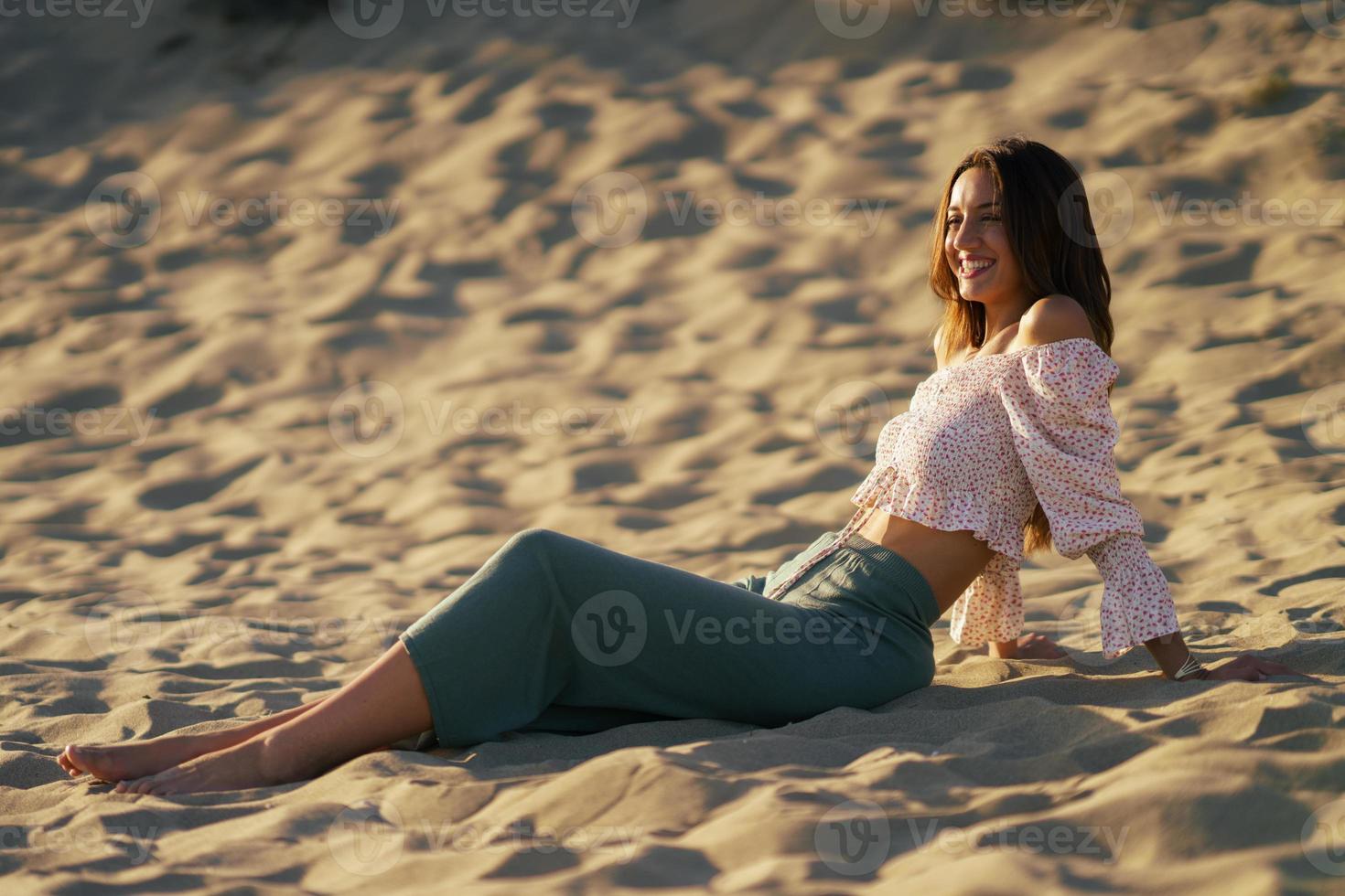 leende kvinna sitter på sanden på stranden foto