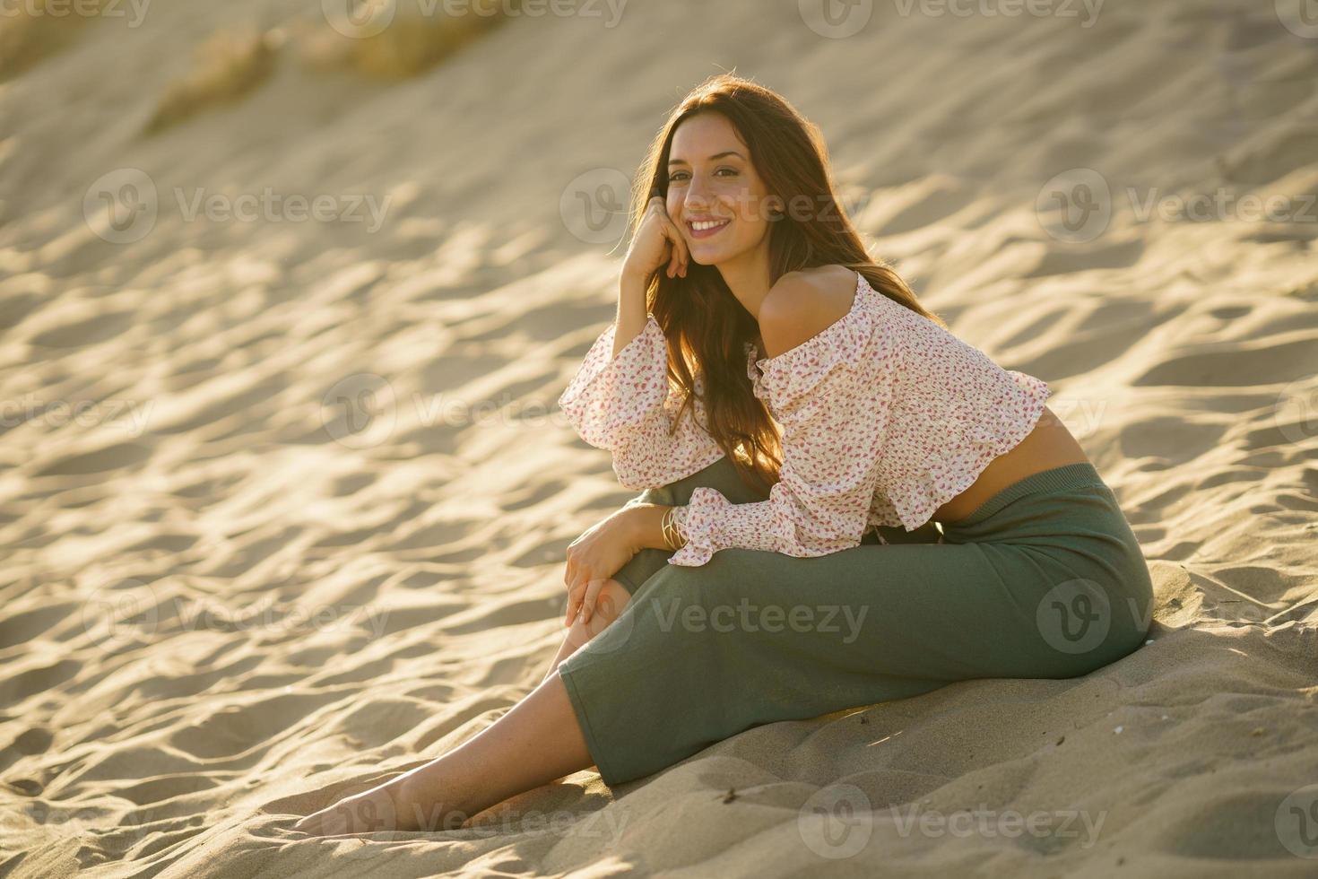 leende kvinna sitter på sanden på stranden foto