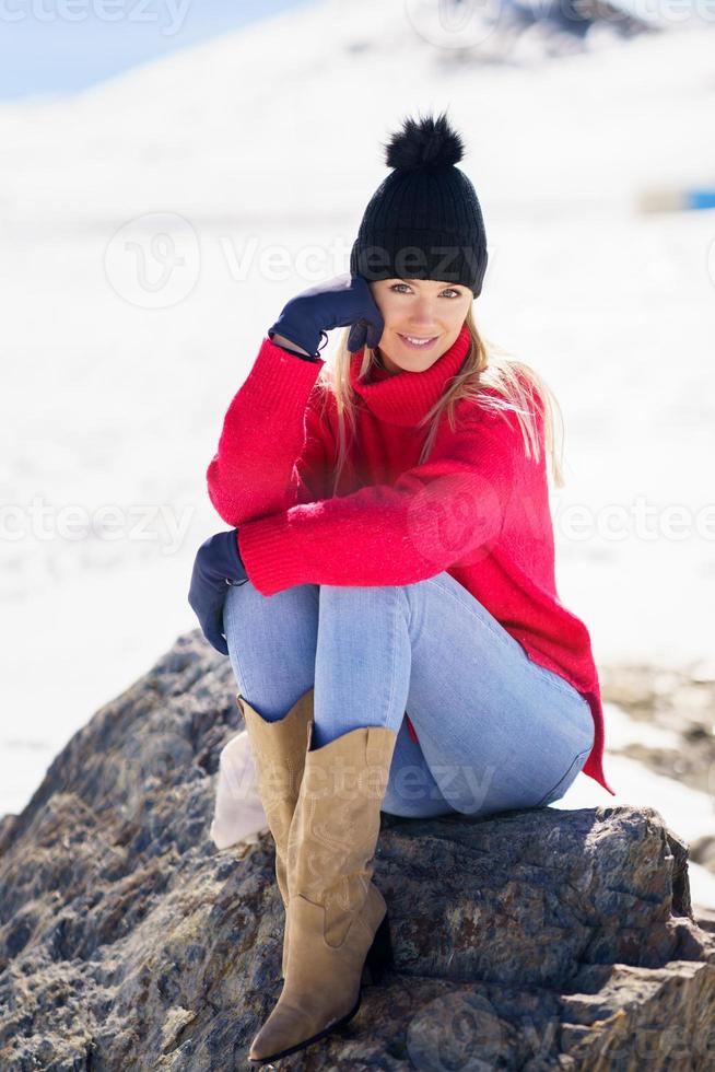 ung kvinna sitter på en sten i de snöiga bergen på vintern, i Sierra Nevada, Granada, Spanien. foto