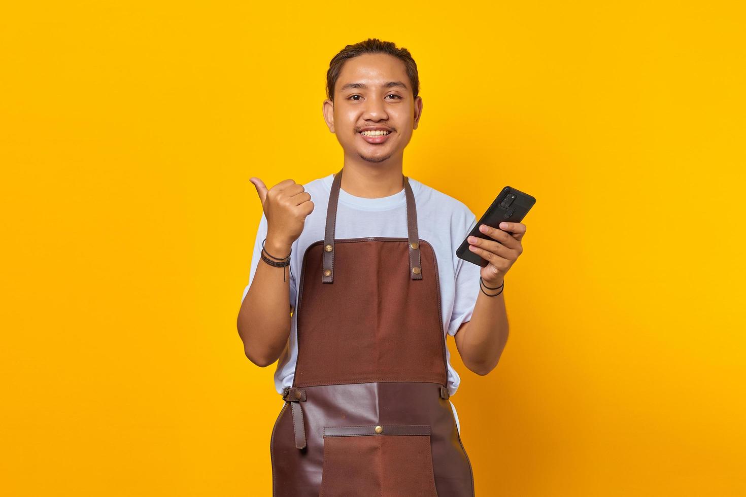 porträtt av glada positiva man håller smartphone med finger visar försäljning rabatt över gul bakgrund foto