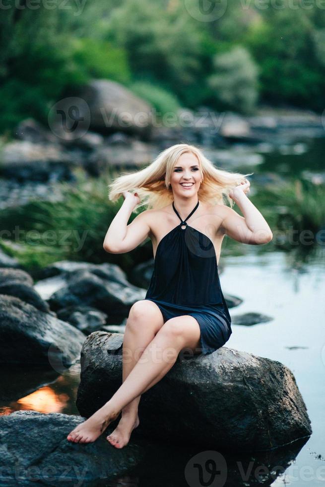 blond flicka i en svart klänning med blå ögon på kusten av floden foto
