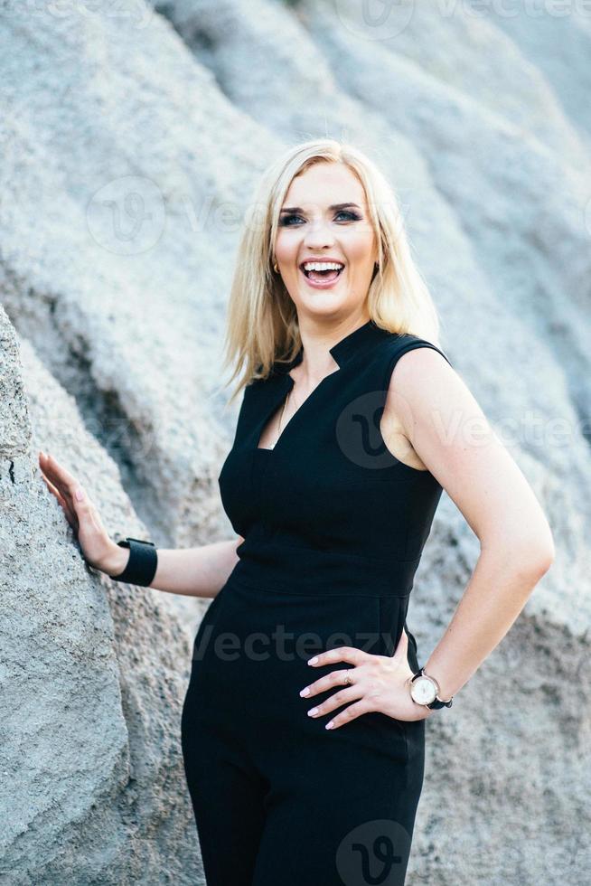 blond tjej i svart byxdräkt med blå ögon på bakgrunden av ett granitbrott foto