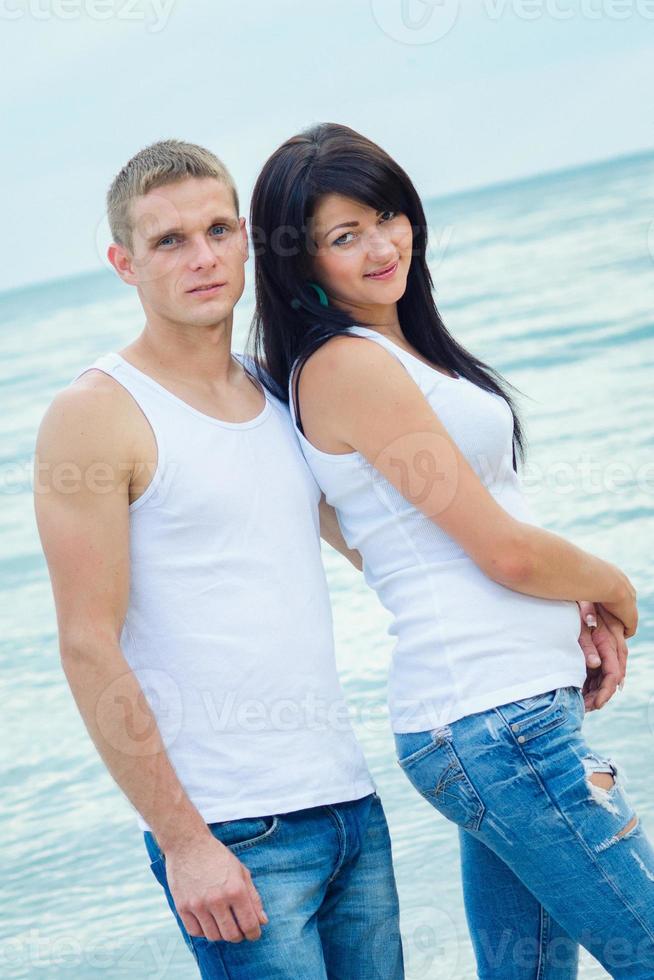 kille och en tjej i jeans och vita t-shirts på stranden foto