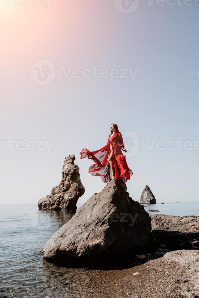 kvinna resa hav. ung Lycklig kvinna i en lång röd klänning Framställ på en strand nära de hav på bakgrund av vulkanisk stenar, tycka om i Island, delning resa äventyr resa foto