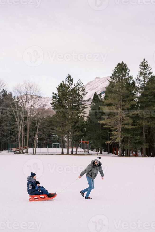 pappa är bärande mamma med en barn på en kälke tvärs över en snöig enkel ser tillbaka. sida se foto