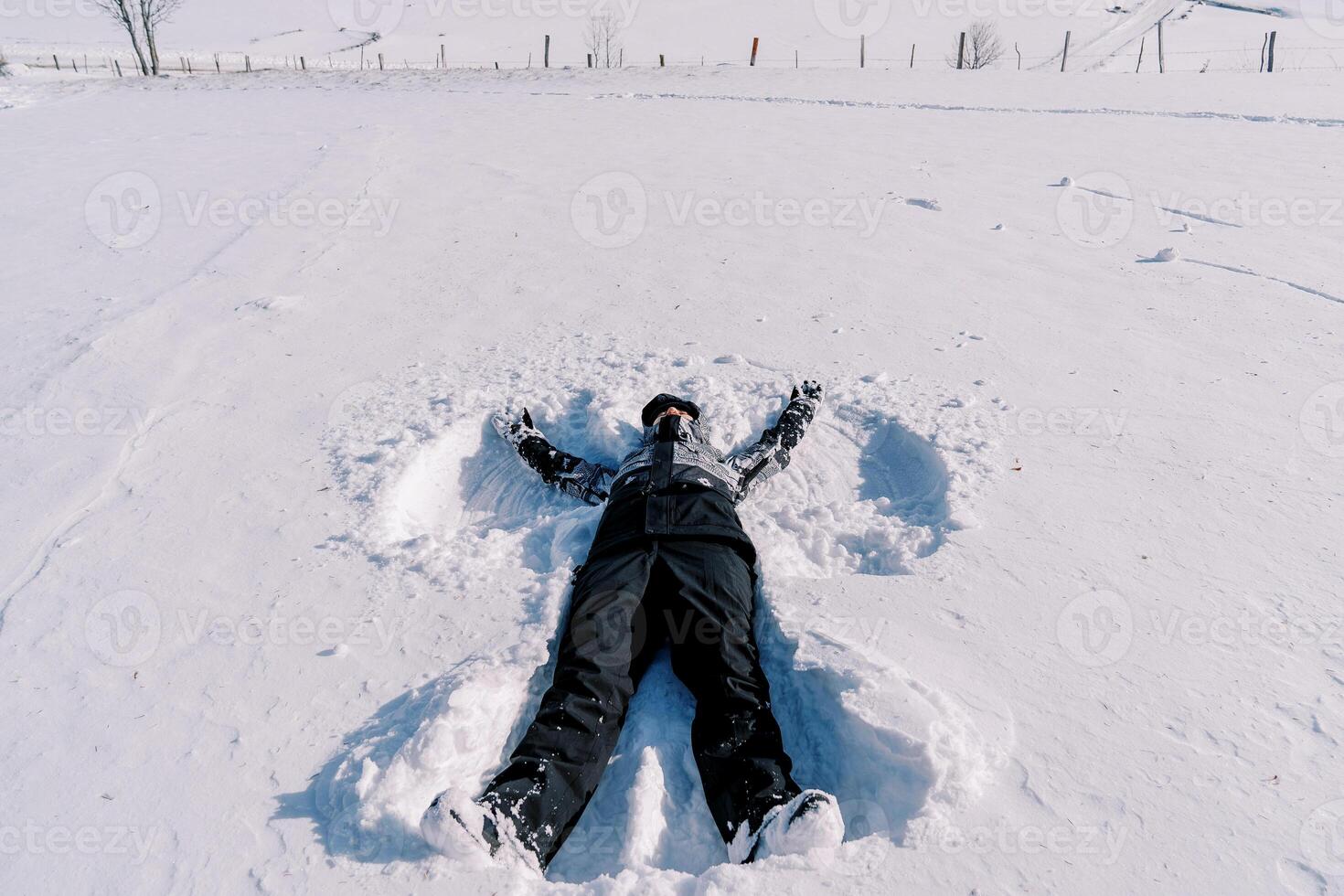 flicka i en åka skidor kostym gör en snö ängel medan liggande på de snö foto