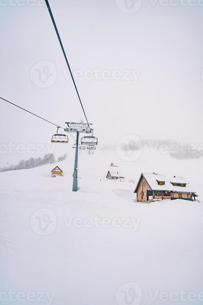 stollift passerar förbi trä- stugor på en snötäckt berg foto