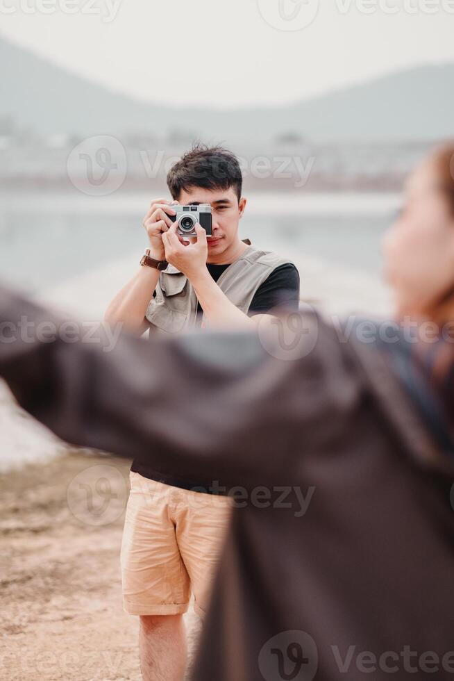 manlig fotograf komponerar en skott med hans årgång kamera, fångande hans ämne i en naturlig sjön miljö. foto